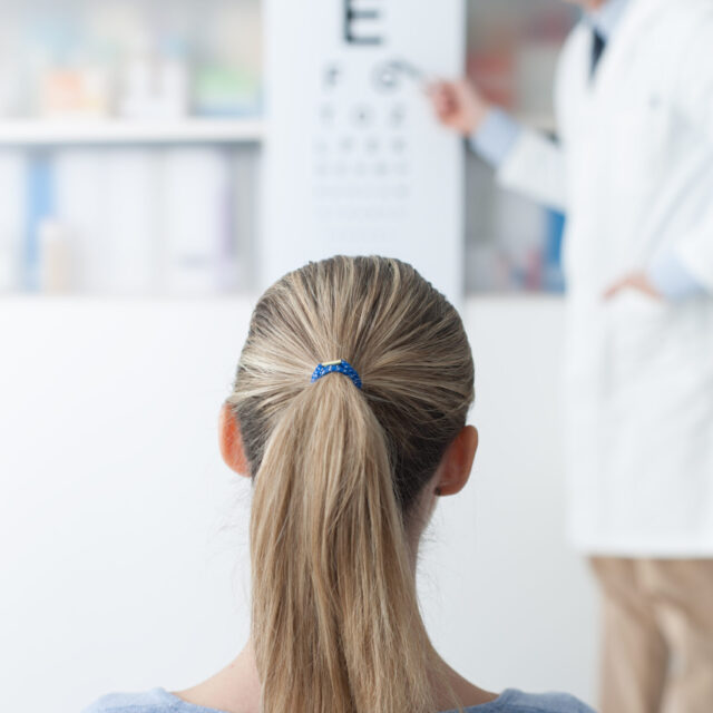 Young woman in the optometrist office examining her eyesight, he is pointing at the chart, eye care concept